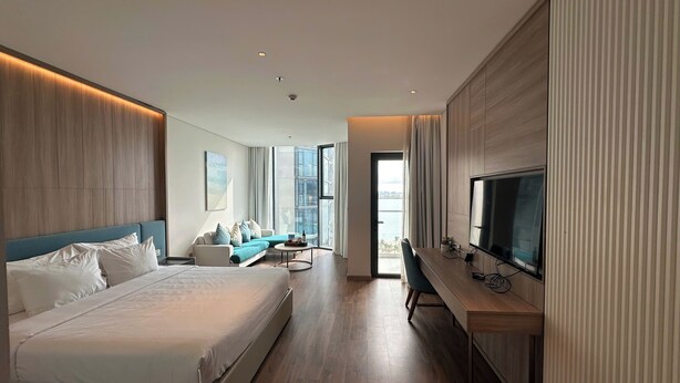 Une chambre d’hôtel moderne dotée d’un grand lit, d’un canapé, d’un bureau avec une télévision et offrant une vue sur la mer.