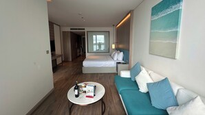 Une chambre d’hôtel moderne, équipée d’un lit, d’un canapé, d’une table basse et d’un tableau représentant une scène de plage.