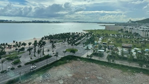 Un paysage urbain côtier avec une plage, une promenade bordée de palmiers et des bâtiments modernes.