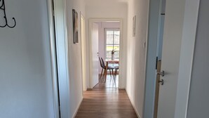Un pasillo con suelo de madera, paredes blancas y puertas que dan a un comedor con una mesa y sillas.