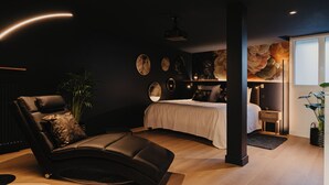 A modern bedroom with a curved ceiling, a bed with white bedding, a black leather chair, and a large mirror on the wall. - Romantic gîte, chic love room: L'alcôve Clisson in the heart of the medieval town (Clisson)