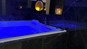 A modern bathroom with a large bathtub, dark marble walls, and a small seating area with a towel. - Romantic gîte, chic love room: L'alcôve Clisson in the heart of the medieval town (Clisson)