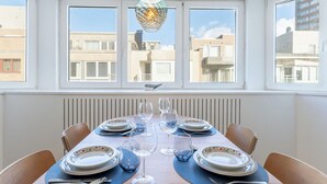 Un comedor con una mesa grande dispuesta para seis personas, ventanas amplias y una lámpara colgante decorativa.