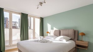 Un dormitorio moderno con una cama grande, una mesita de noche y vistas de la ciudad a través de una puerta corrediza.