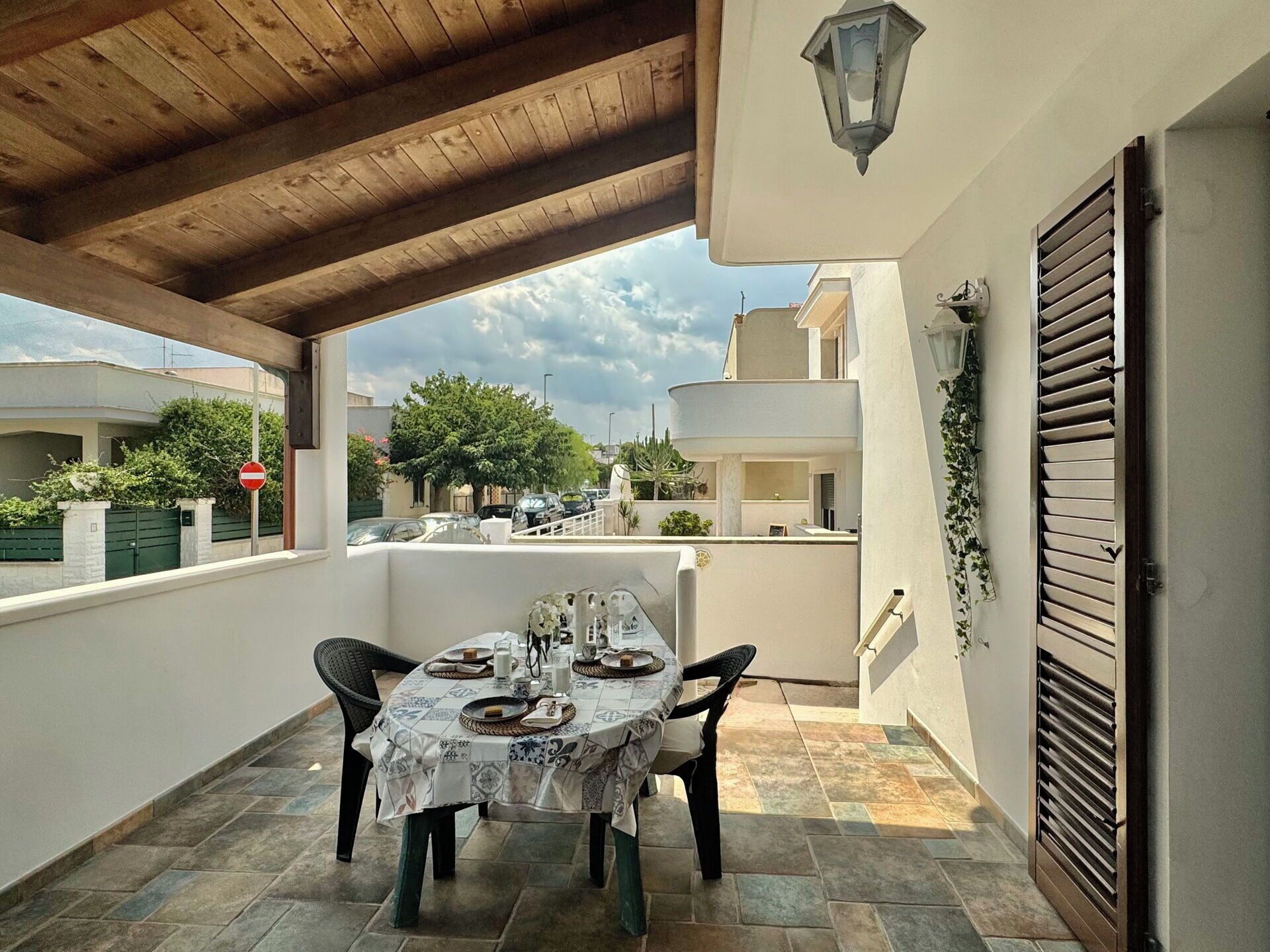 A covered outdoor patio with a table set for dining, a wooden ceiling, and a view of the neighborhood.