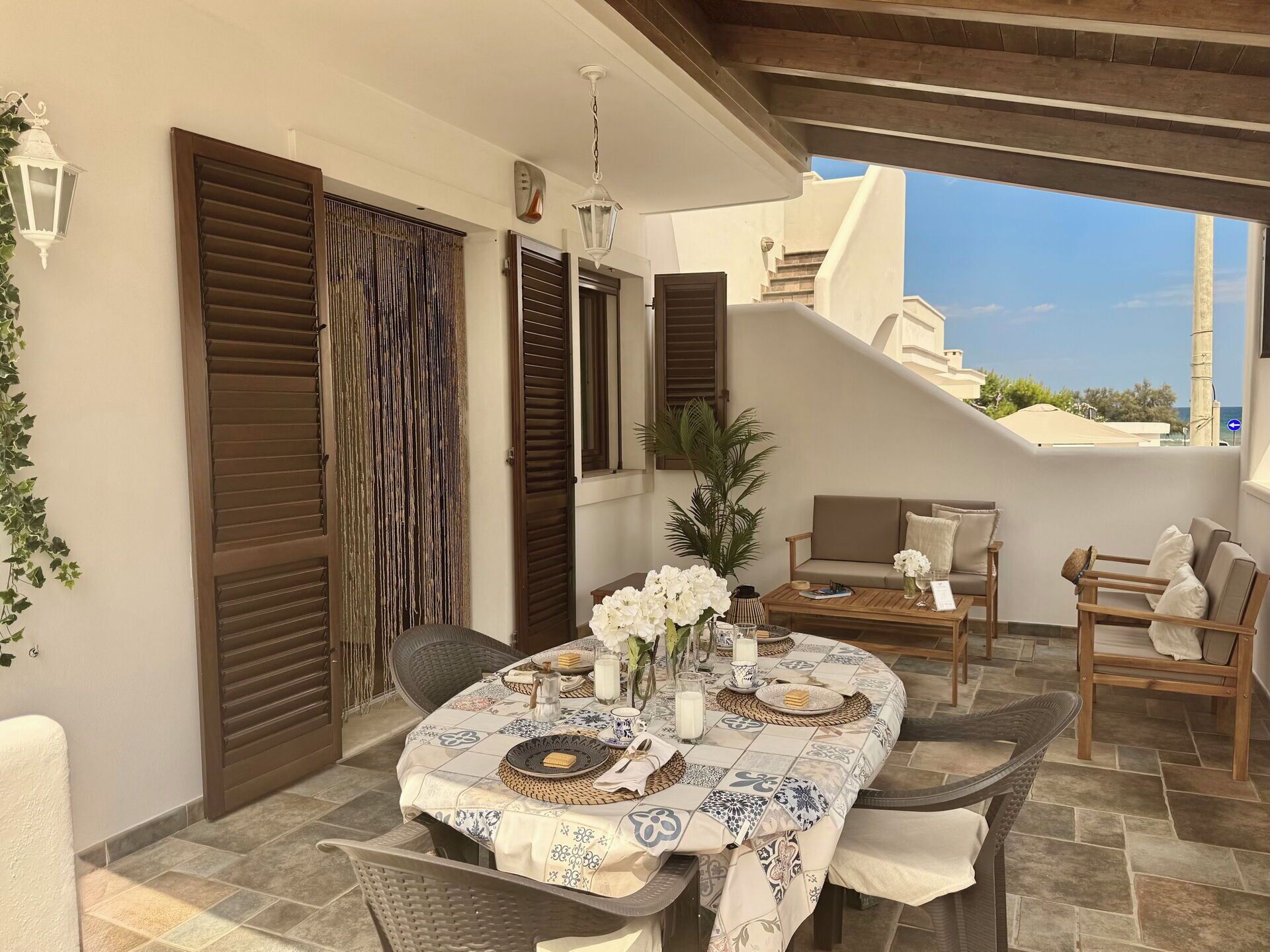 Eine Terrasse mit rundem Esstisch, umgeben von Korbstühlen und einer Couch.