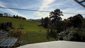 Una habitación con un amplio ventanal que da a un paisaje verde, suelo de hormigón y barandilla de metal.