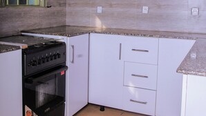 A kitchen with white cabinets, a black stove, and tiled flooring. - Breeze House Gikondo (Kigali)