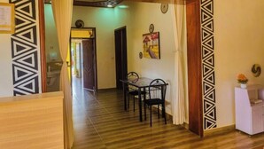 A room with a wooden floor, a dining table with chairs, a white cabinet, and a patterned wall. - Breeze House Gikondo (Kigali)