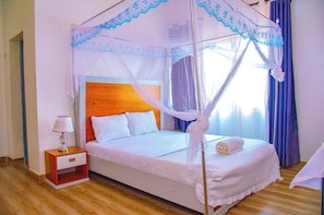 A bed with a canopy, a bedside table with a lamp, and a window with curtains. - Breeze House Gikondo (Kigali)