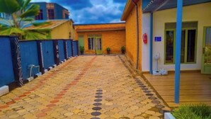 A courtyard with a patterned tile floor, a blue fence, and a building with a green door. - Breeze House Gikondo (Kigali)