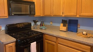 A kitchen with wooden cabinets, a black stove, a microwave, and a blue countertop. - Mermaid's and Mutts Retreat - 30 Day Listing (Norfolk)