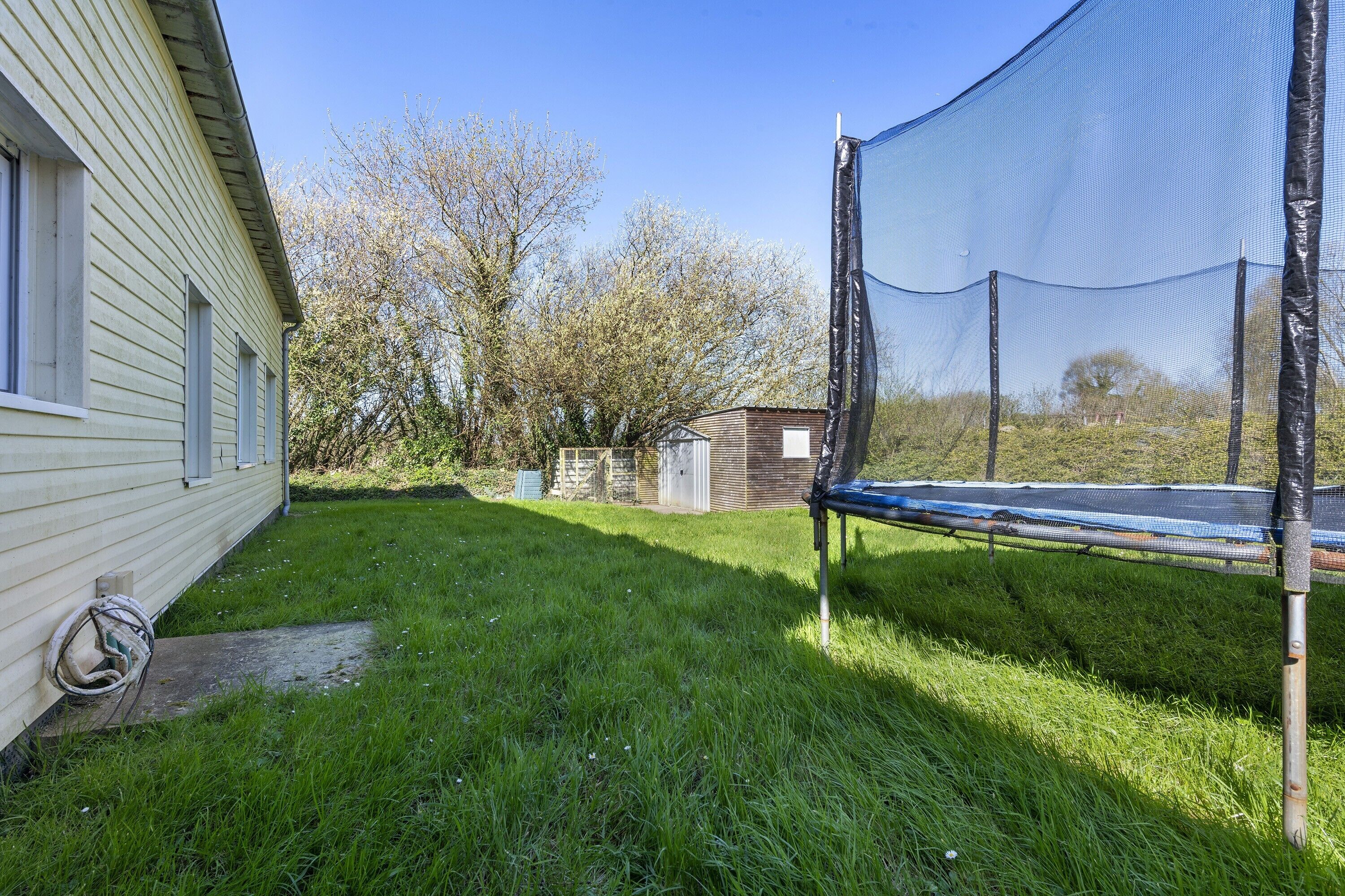 Un jardin avec un trampoline, un abri de jardin et une maison.