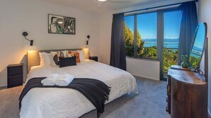 Une chambre avec un grand lit, un ventilateur de plafond, une table de chevet, une commode, un tableau et une vue sur la mer.