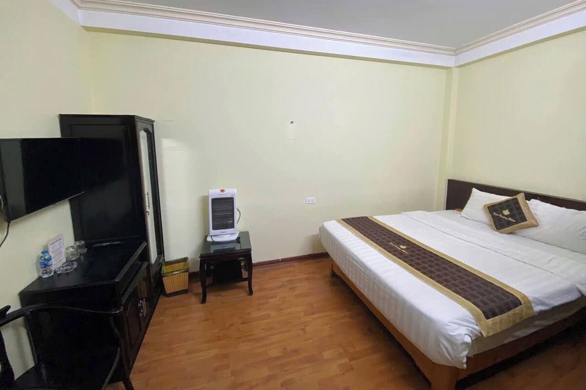 Habitación de hotel con una cama, televisión, una mesita con lámpara y suelo de madera.