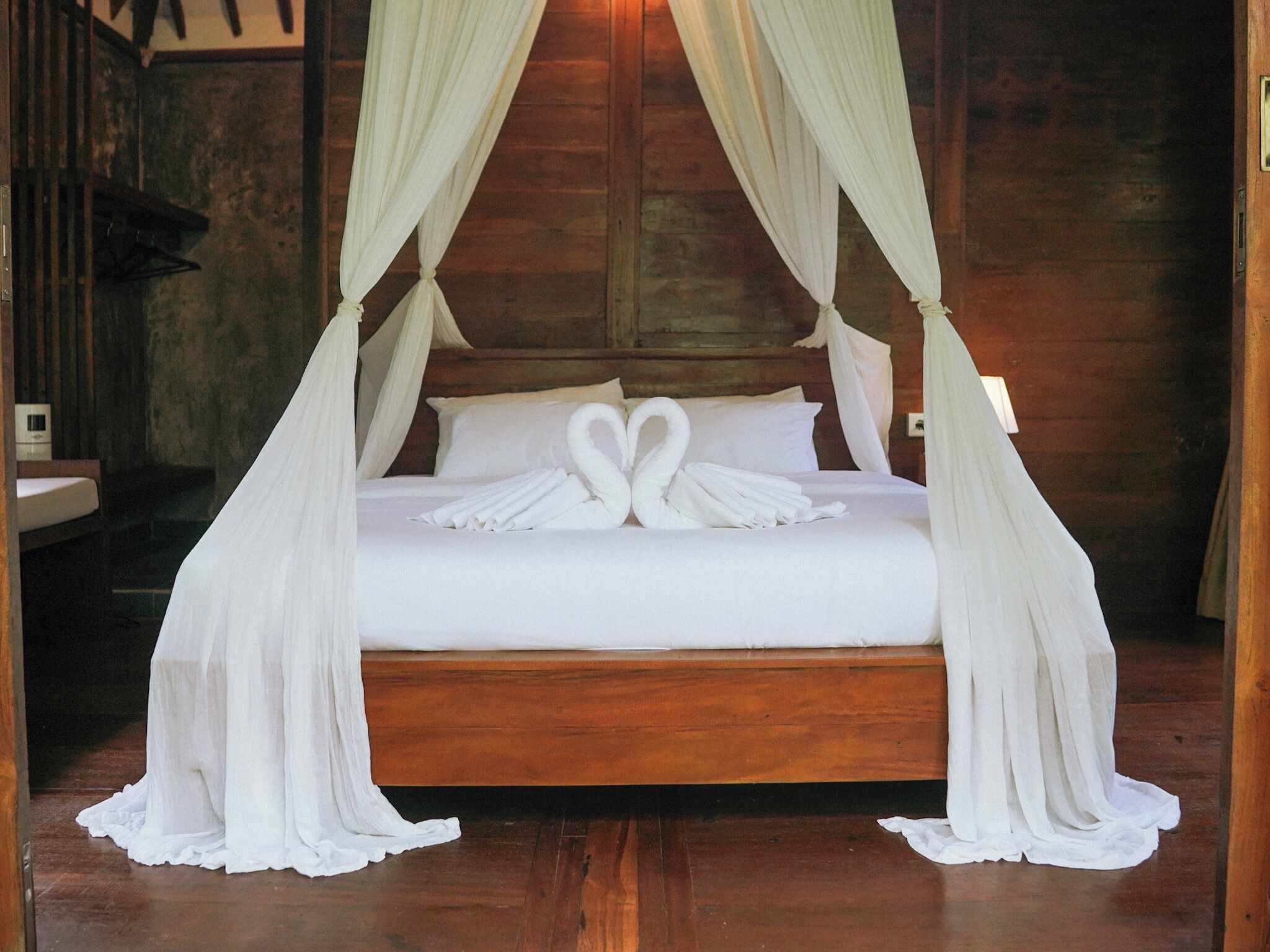 A bed with a canopy, white linens, and two swan-shaped towels.