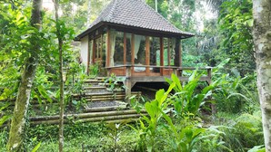 Une structure en bois surmontée d’un toit en tuiles, entourée d’une végétation luxuriante et d’arbres.