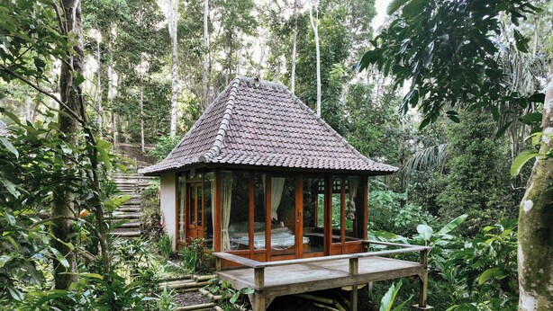 Un belvédère en bois, surmonté d’un toit en tuiles, entouré d’une végétation luxuriante et d’arbres.
