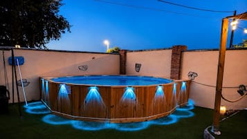 Una bañera de hidromasaje de madera con luces LED azules alrededor de su borde, sobre césped artificial.