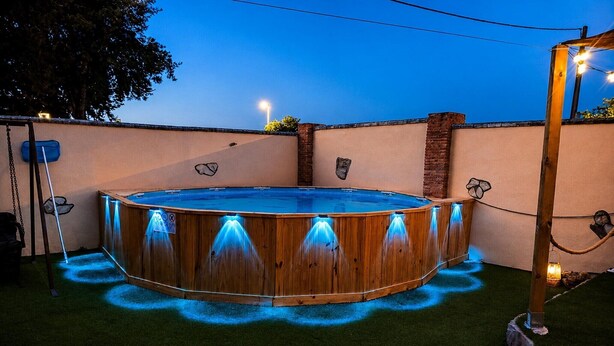 A wooden hot tub with built-in lighting, surrounded by artificial grass and a brick wall. - Chalet in Rivero de Posadas with Pool (Rivero de Posadas)
