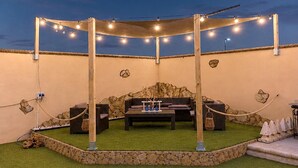 An outdoor patio area with a covered seating arrangement, string lights, and a stone wall backdrop. - Chalet in Rivero de Posadas with Pool (Rivero de Posadas)