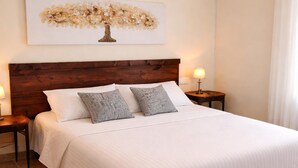 A neatly made bed with a wooden headboard, two bedside tables with lamps, and a wall-mounted artwork of a tree. - Chalet in Rivero de Posadas with Pool (Rivero de Posadas)