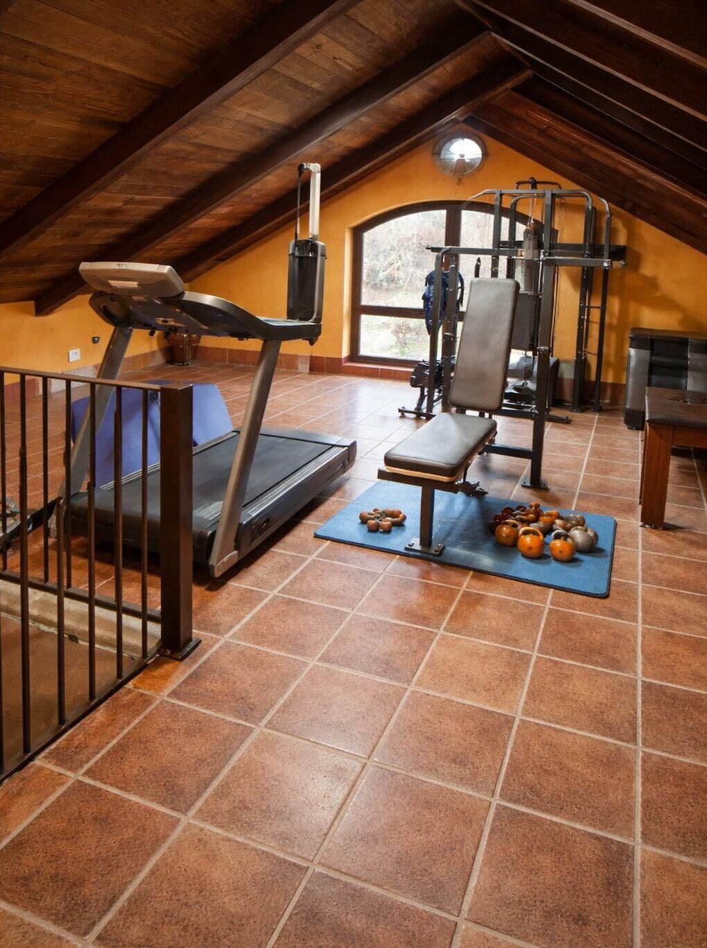 An attic gym with a treadmill, bench, kettlebells, and a pull-up bar.