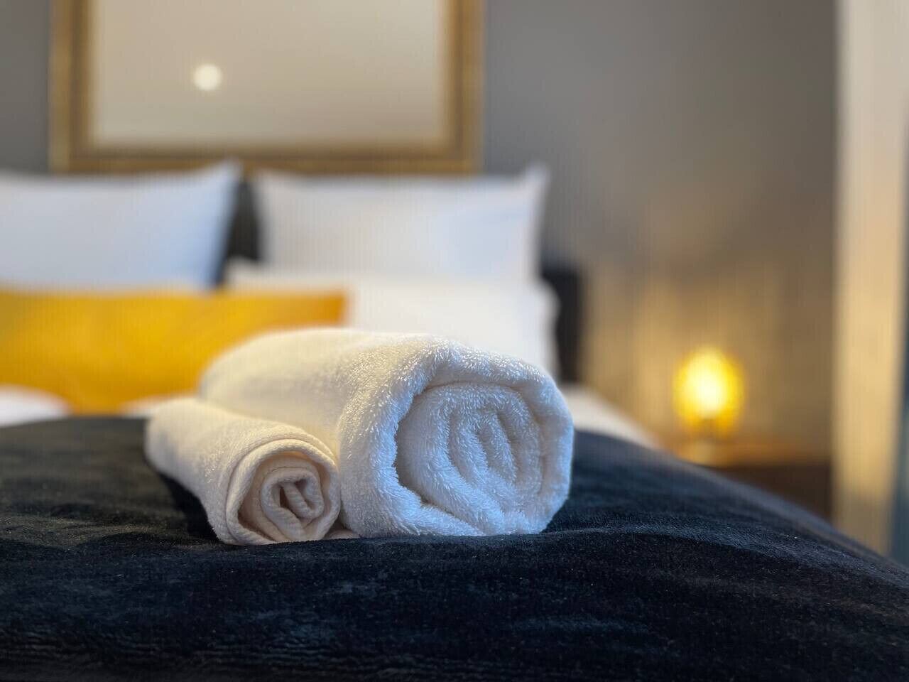 A neatly made bed with a rolled white towel and a dark-colored blanket.