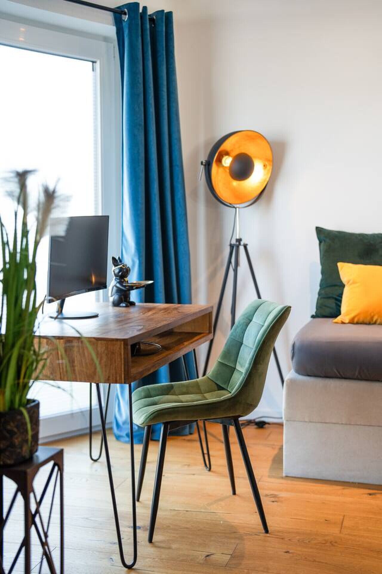 En moderne stue med et træskrivebord, en grøn lænestol, en gulvlampe og en sofa med puder.