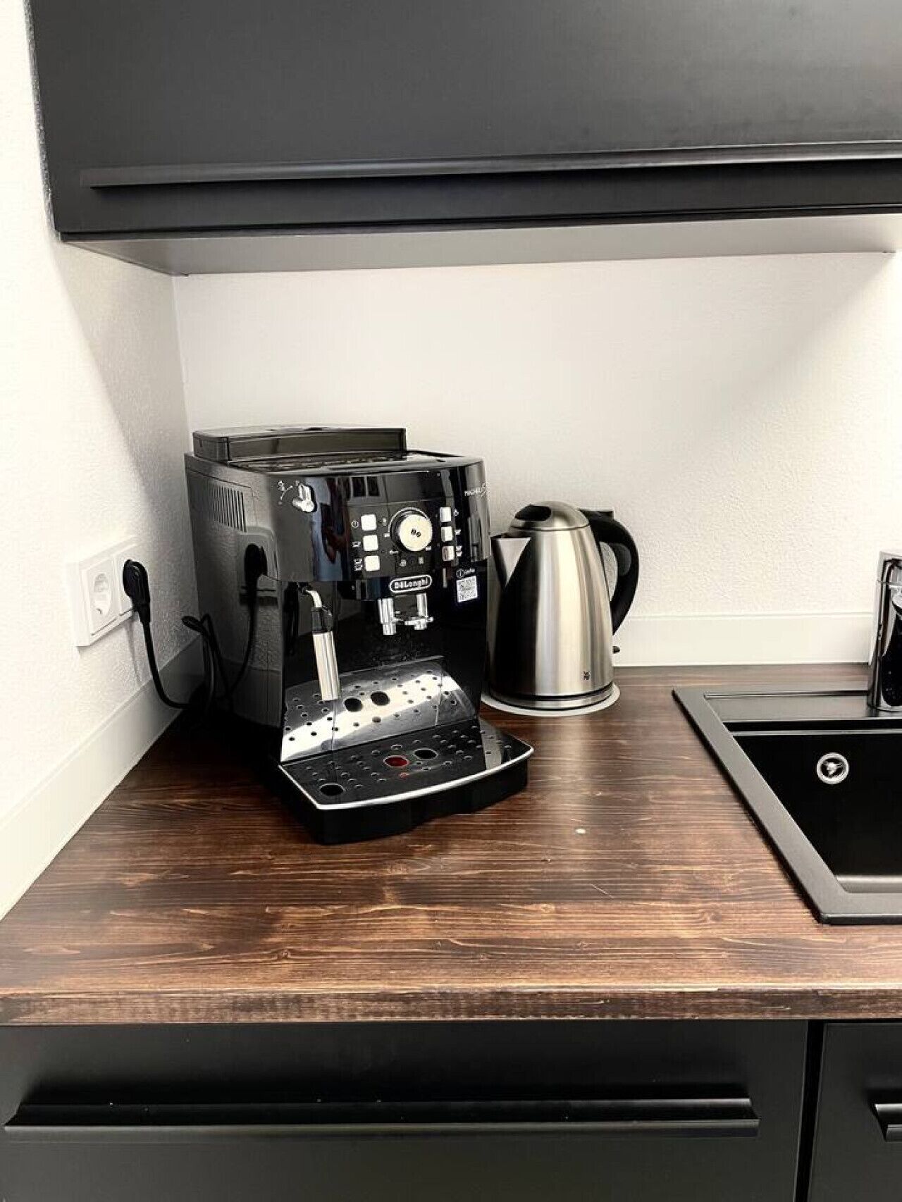 A kitchen with a coffee machine, a kettle, and a sink.