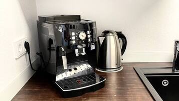 A kitchen with a coffee machine, a kettle, and a sink.