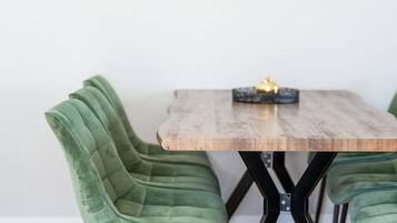 A dining table with a wooden top and black metal legs, flanked by two green upholstered chairs. Above the table, there are two framed botanical prints on the wall.