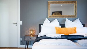 A hotel room with a bed, a nightstand with a lamp, a mirror on the wall, and a door. - 90m2 Loft I Kaffee I Terrasse I E-Parkplatz (Rosenheim)