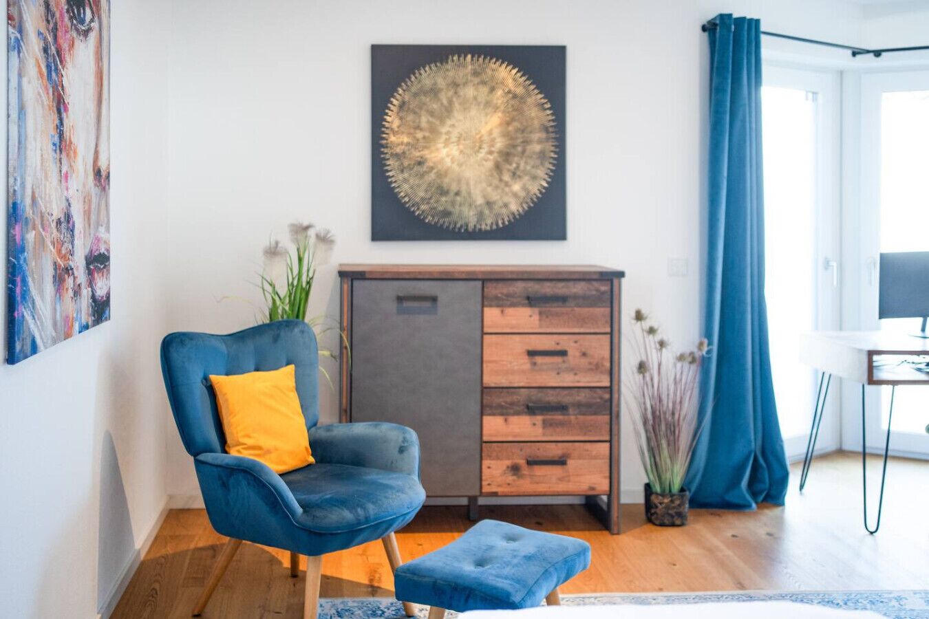 Ein stilvolles Wohnzimmer mit blauem Sessel, Holzschrank und großem abstrakten Gemälde.