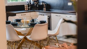 A modern kitchen with white cabinets, a black countertop, and a dining area with a glass table and white chairs. - YAYstay - 58m2 I balkony I 56` Smart TV I train (Mühldorf am Inn)