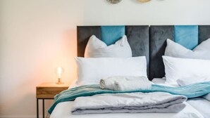 A neatly made bed with white and gray linens, a teal throw blanket, and a rolled towel. - YAYstay - 58m2 I balkony I 56` Smart TV I train (Mühldorf am Inn)