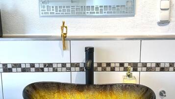 A bathroom with a large, oval vessel sink, a wall-mounted mirror, and a towel rack.