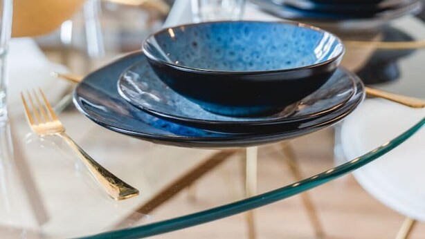 A dining table set with blue plates and gold cutlery, glasses, and a glass vase. - YAYstay - 58m2 I balkony I 56` Smart TV I train (Mühldorf am Inn)