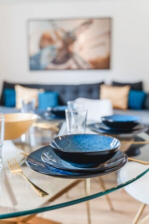 A dining table set with blue plates and gold cutlery, glasses, and a glass vase. - YAYstay - 58m2 I balkony I 56` Smart TV I train (Mühldorf am Inn)