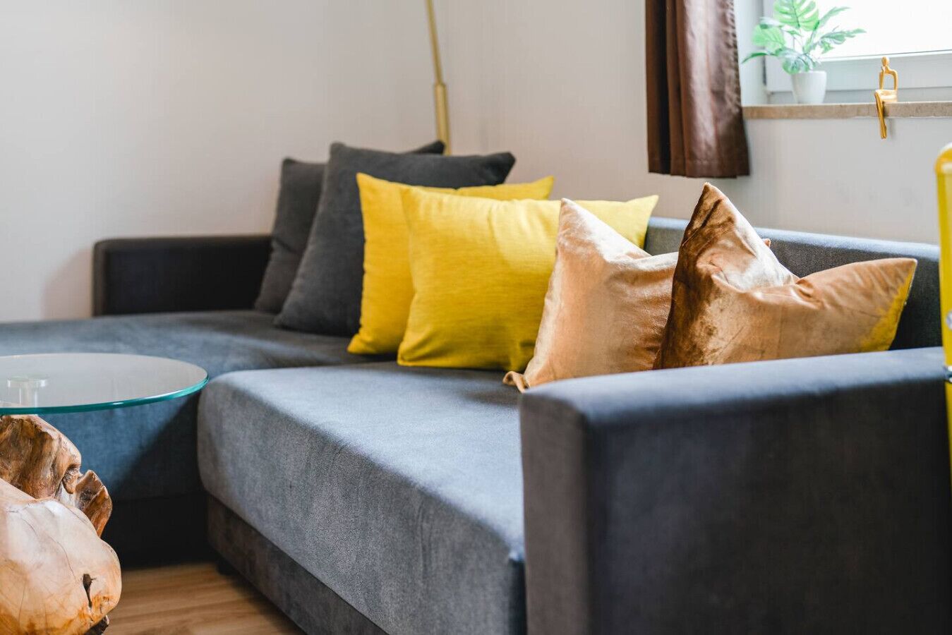 A modern living room with a grey sofa, yellow and brown cushions, and a glass coffee table.