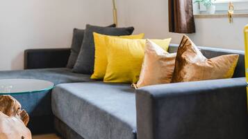 A modern living room with a grey sofa, yellow and brown cushions, and a glass coffee table.