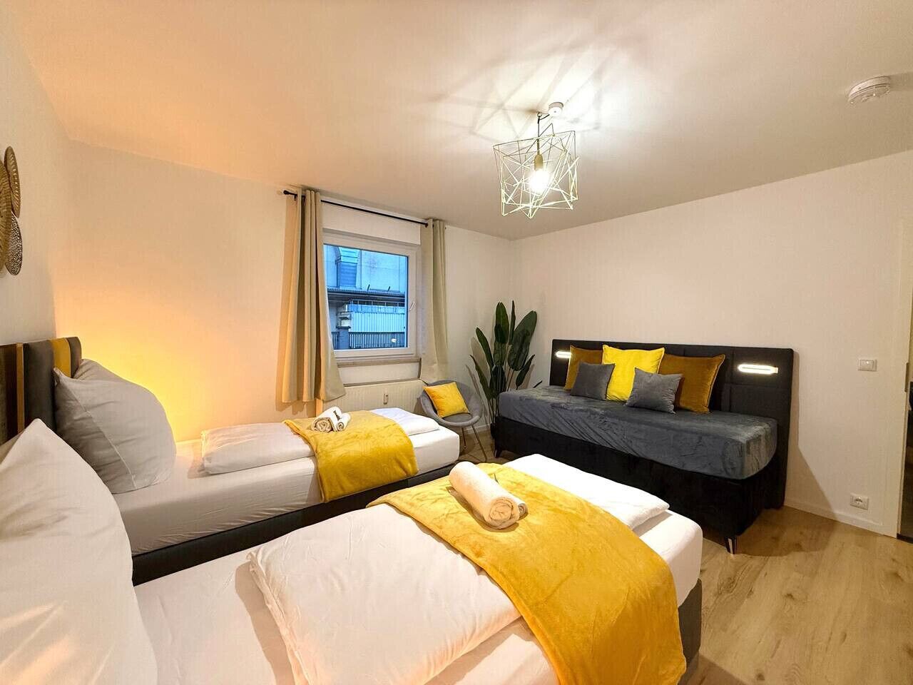 Une chambre d’hôtel avec deux lits, une grande fenêtre, une plante et un luminaire moderne.
