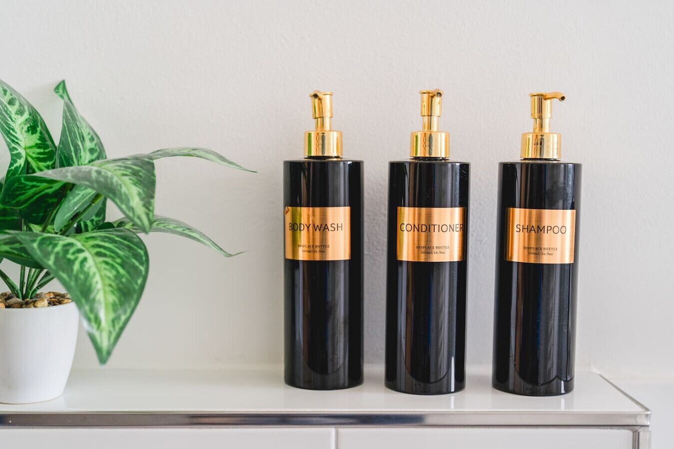 Tres botellas negras con etiquetas doradas sobre una superficie blanca.