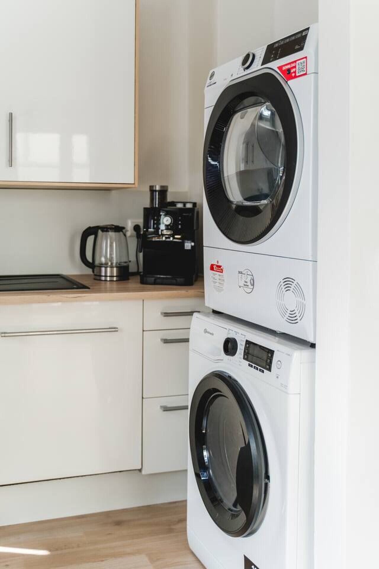 A compact kitchen with a stacked washer and dryer, a coffee maker, and a kettle on the countertop.