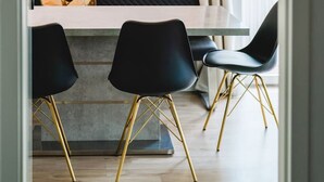 Un comedor moderno con diseño minimalista, que presenta una mesa central con dos sillas negras y un banco. Sobre la mesa, un reloj de pared único con números romanos y una lámpara colgante.