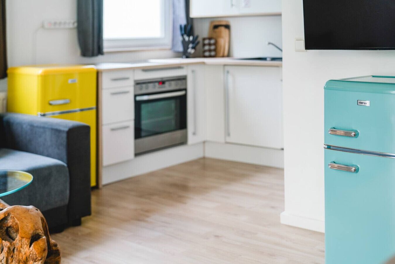 Una cocina compacta con armarios blancos, un electrodoméstico amarillo y un refrigerador verde azulado.
