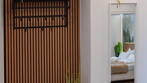 Un intérieur moderne avec un mur à lattes de bois, un banc, une plante en pot et un miroir encadré qui reflète une chambre à coucher.