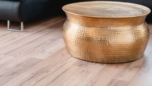 Un salon moderne avec un canapé d’angle gris foncé, une table basse ronde en laiton et un plancher en bois.
