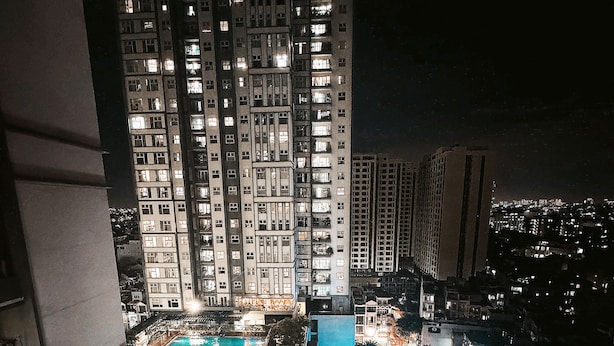 A high-rise building with multiple floors, a swimming pool, and a street with parked cars.