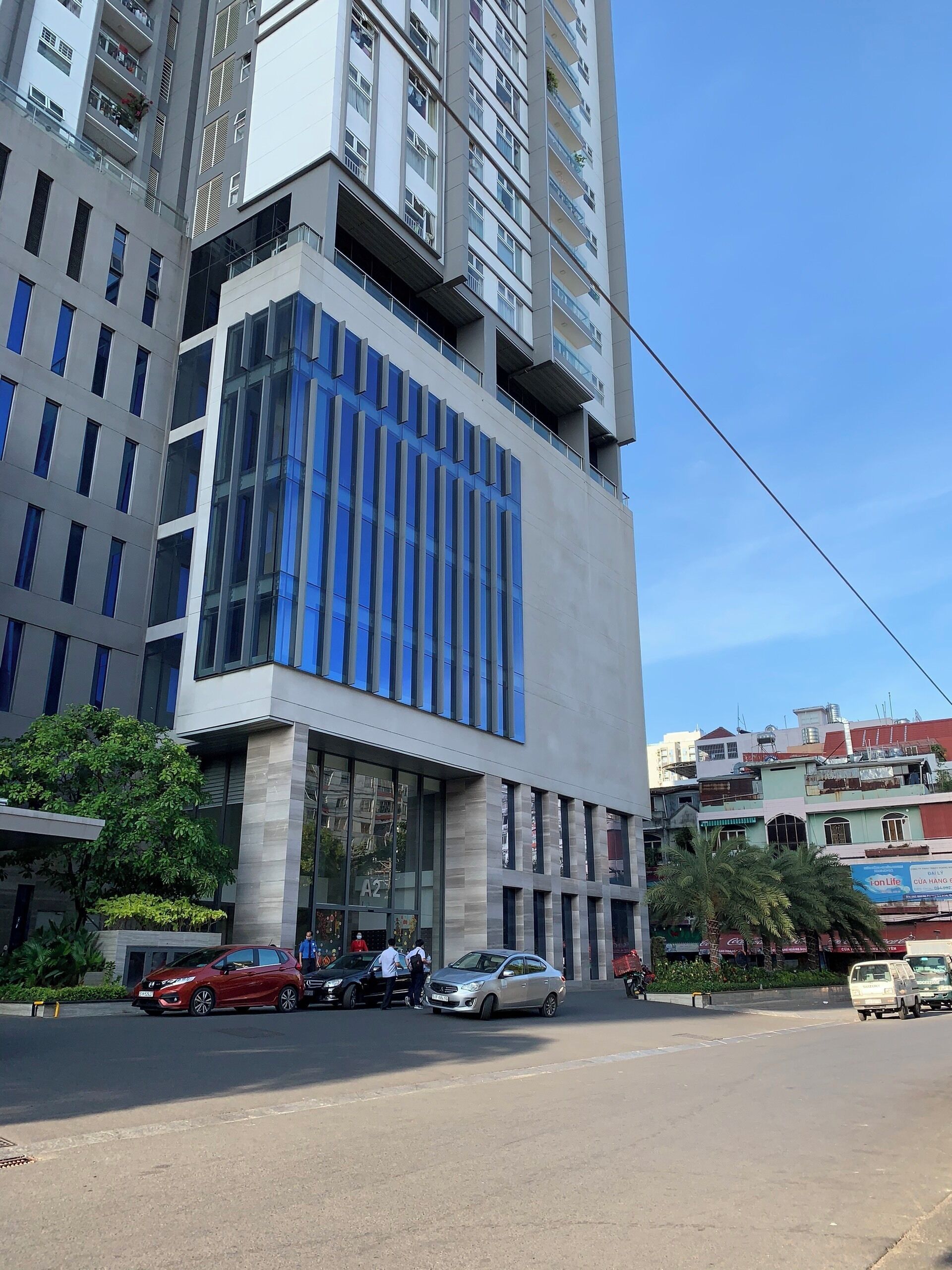 Un bâtiment moderne doté d’une façade en verre, de nombreux balcons et d’un espace de stationnement où sont garées des voitures.